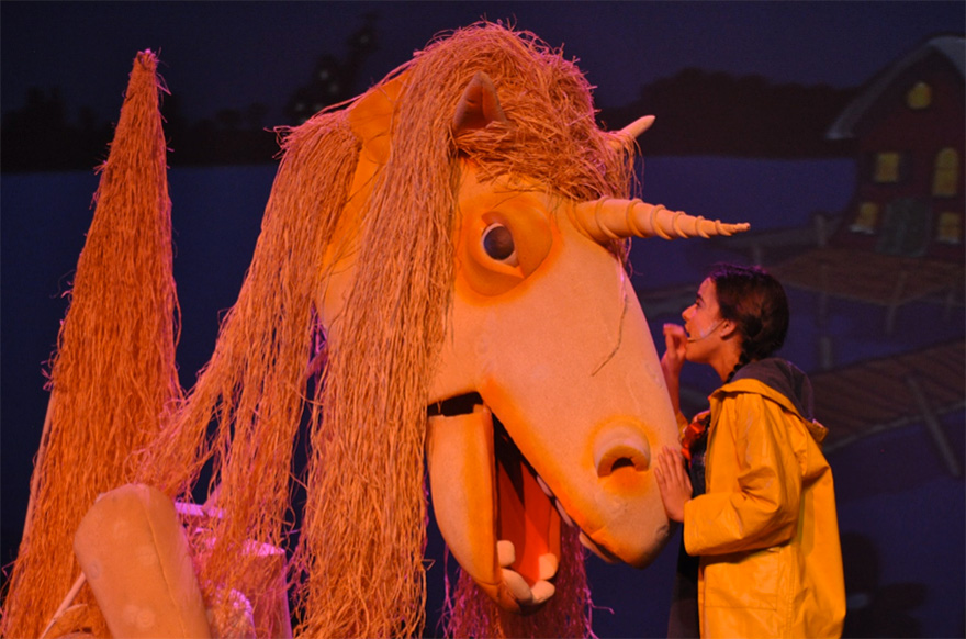 una niña hablándole a un unicornio gigante en un teatro